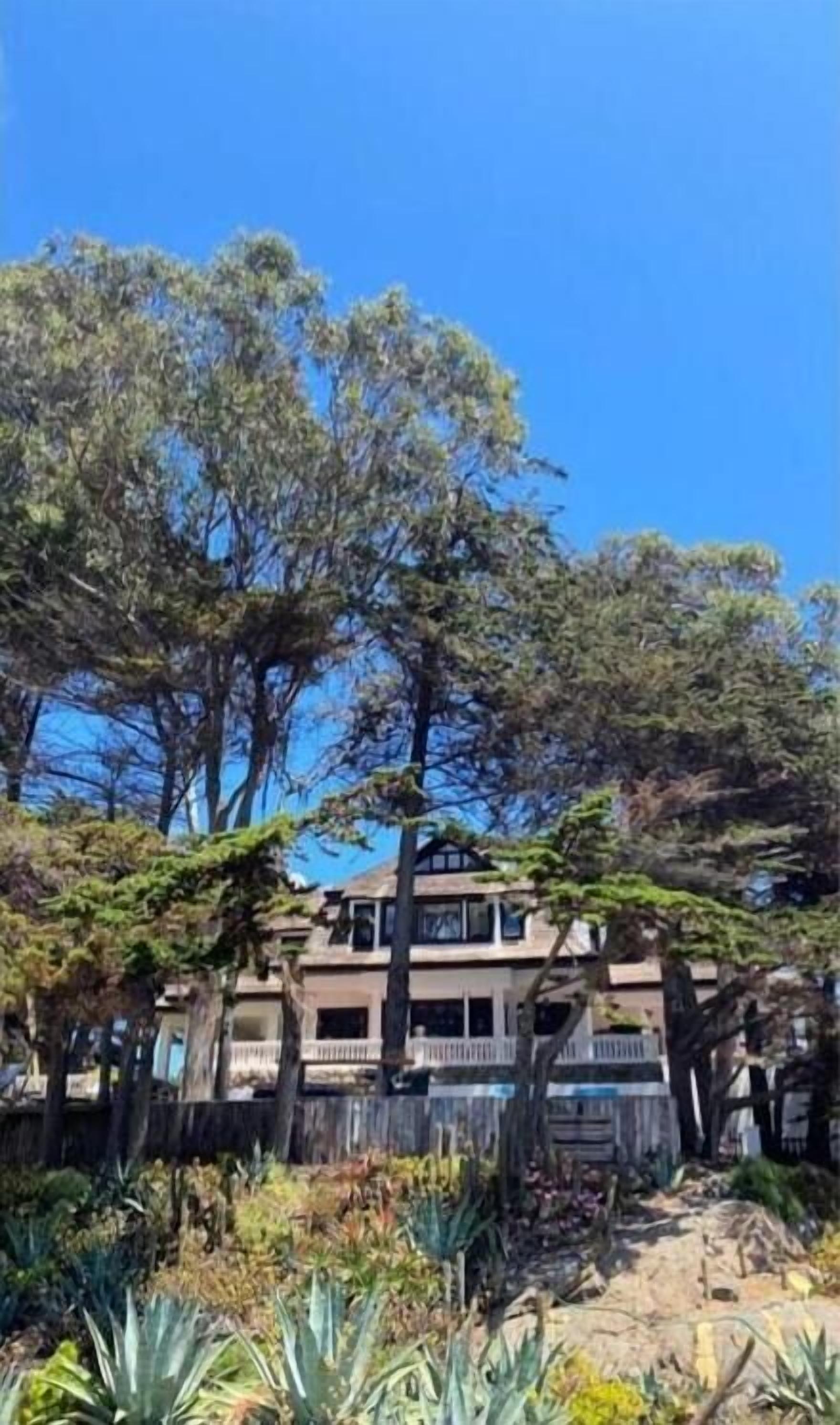 A two-story building with a balcony, surrounded by trees and plants.