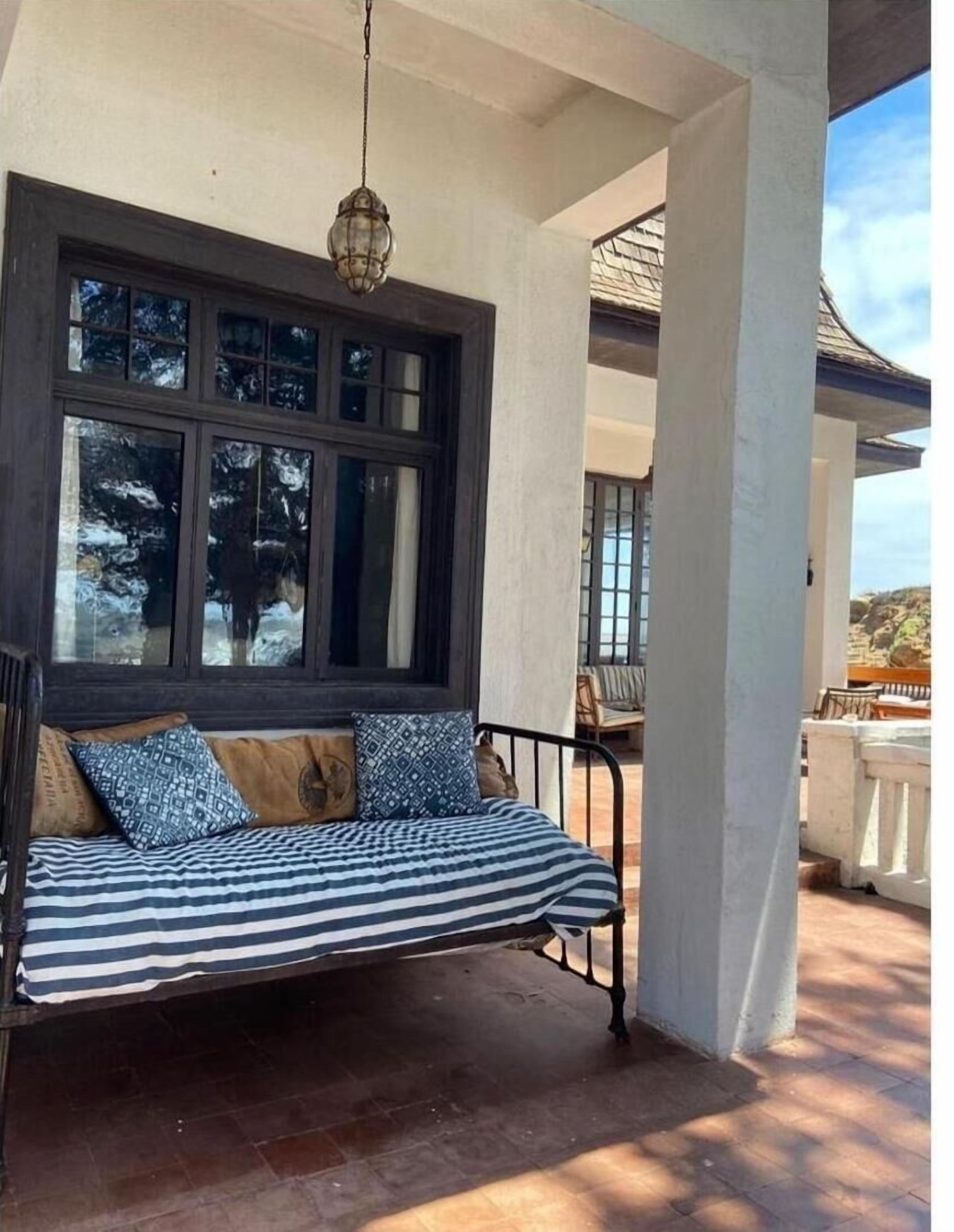 A covered outdoor seating area with a swing seat, large windows, and a hanging light fixture.