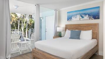 Un dormitorio con cama de madera, ropa de cama blanca, un cuadro de barcos de pesca y vistas a palmeras a través de la puerta.