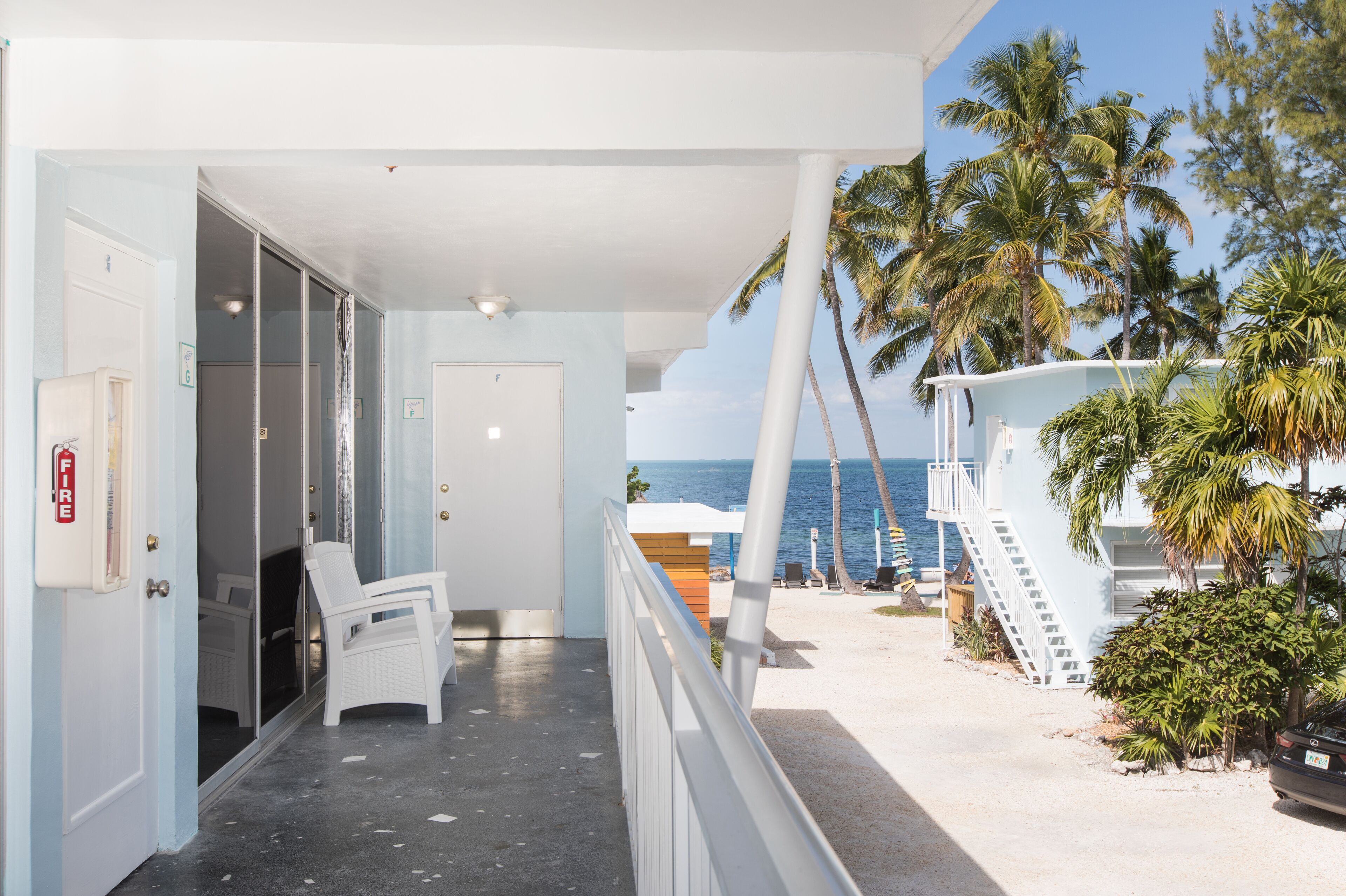 Een balkon met uitzicht op de oceaan, een brandblusser en een stoel.