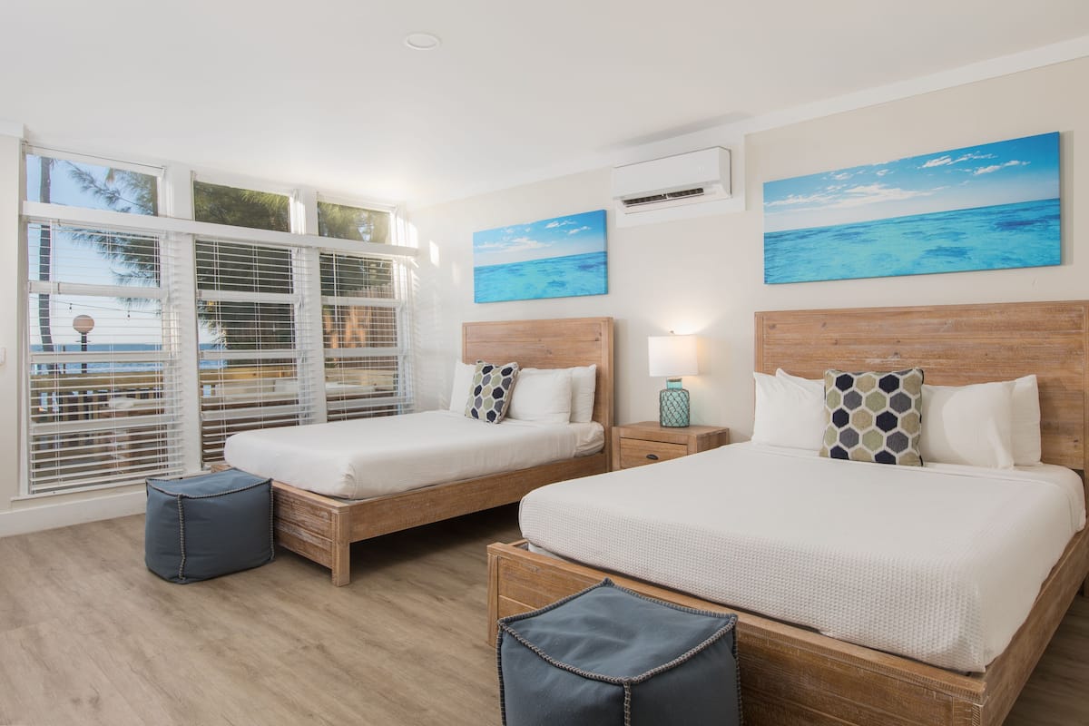 A hotel room with two beds, a view of the ocean through large windows, and artwork on the walls.