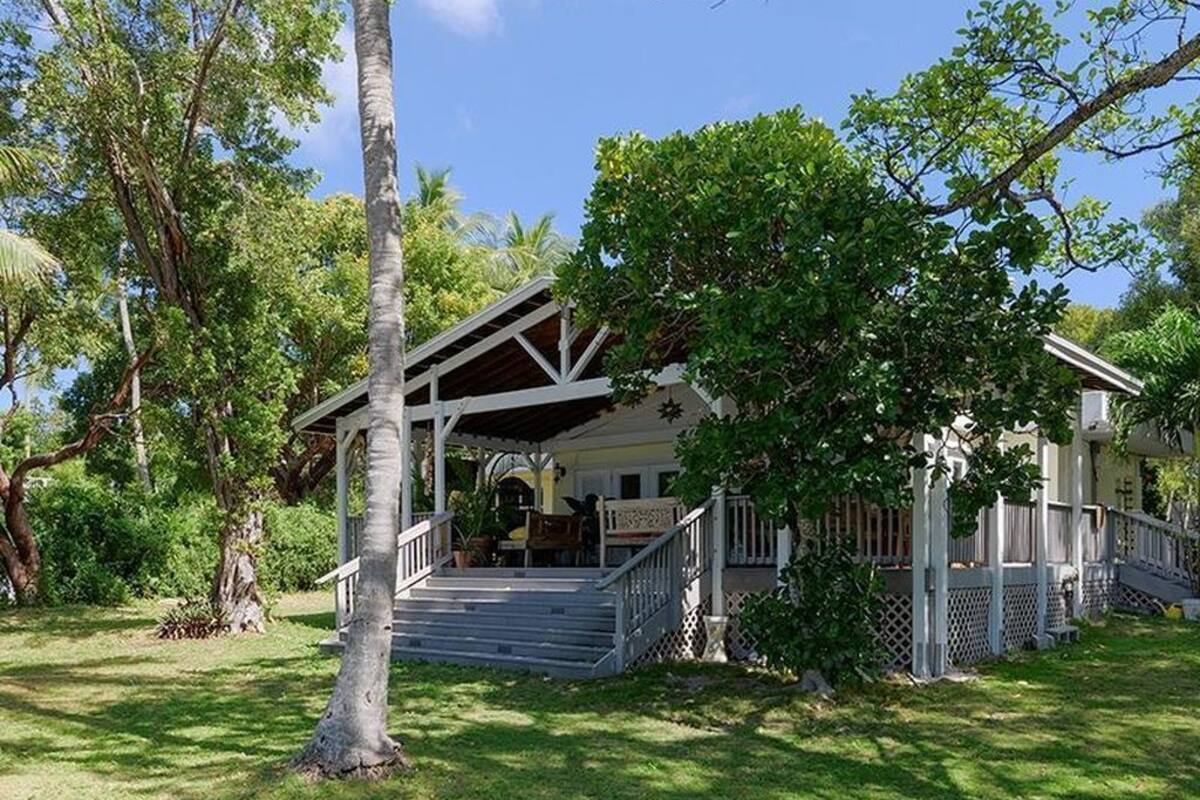A two-story house with a porch, surrounded by lush greenery and trees.
