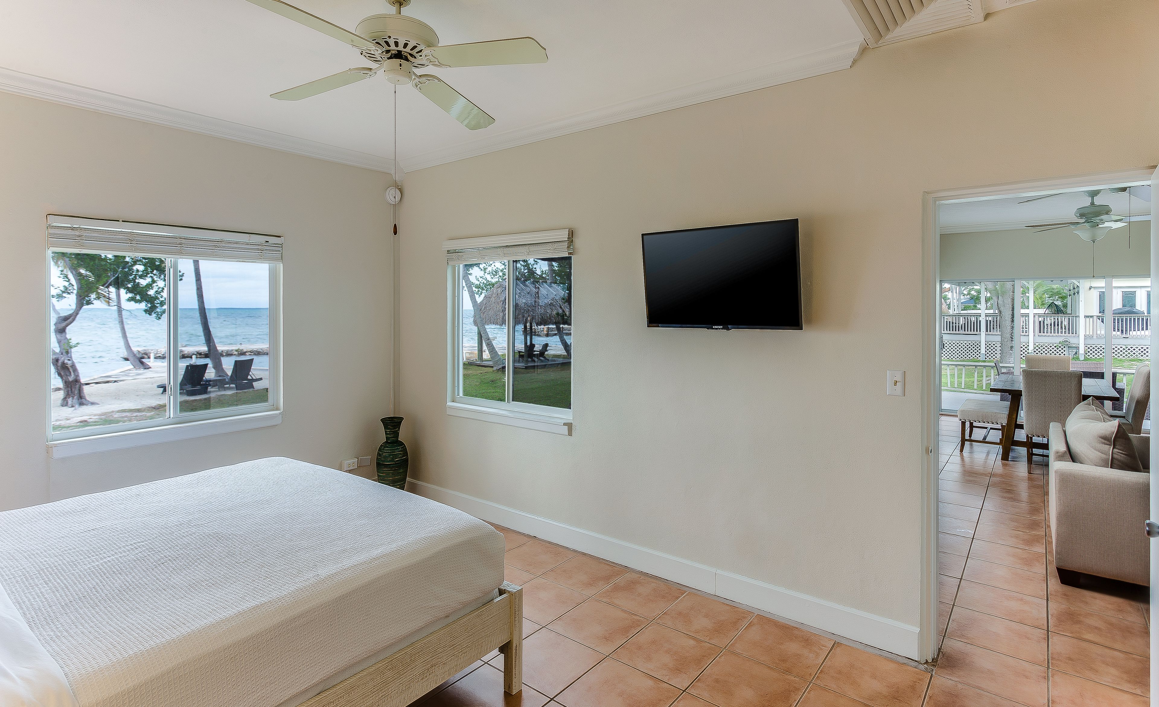 A bedroom with a bed, a TV, and two windows with a view of the beach.