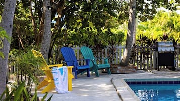 A poolside area with a pool, lounge chairs, and a grill.