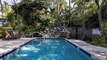 A swimming pool with a stone wall and a wooden fence in the background.