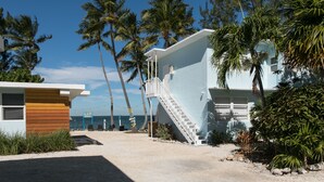 A beachfront property with a staircase leading to a light blue building, palm trees, and a clear view of the ocean. - La Jolla Resort (Islamorada)