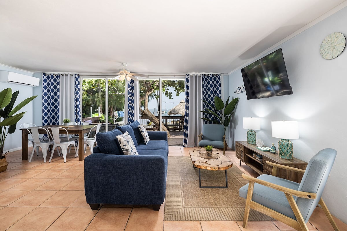 A living room with a blue sofa, a wooden coffee table, and a TV mounted on the wall.