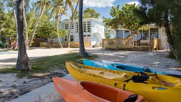 A beachside resort with kayaks, palm trees, and a building with a deck and stairs.