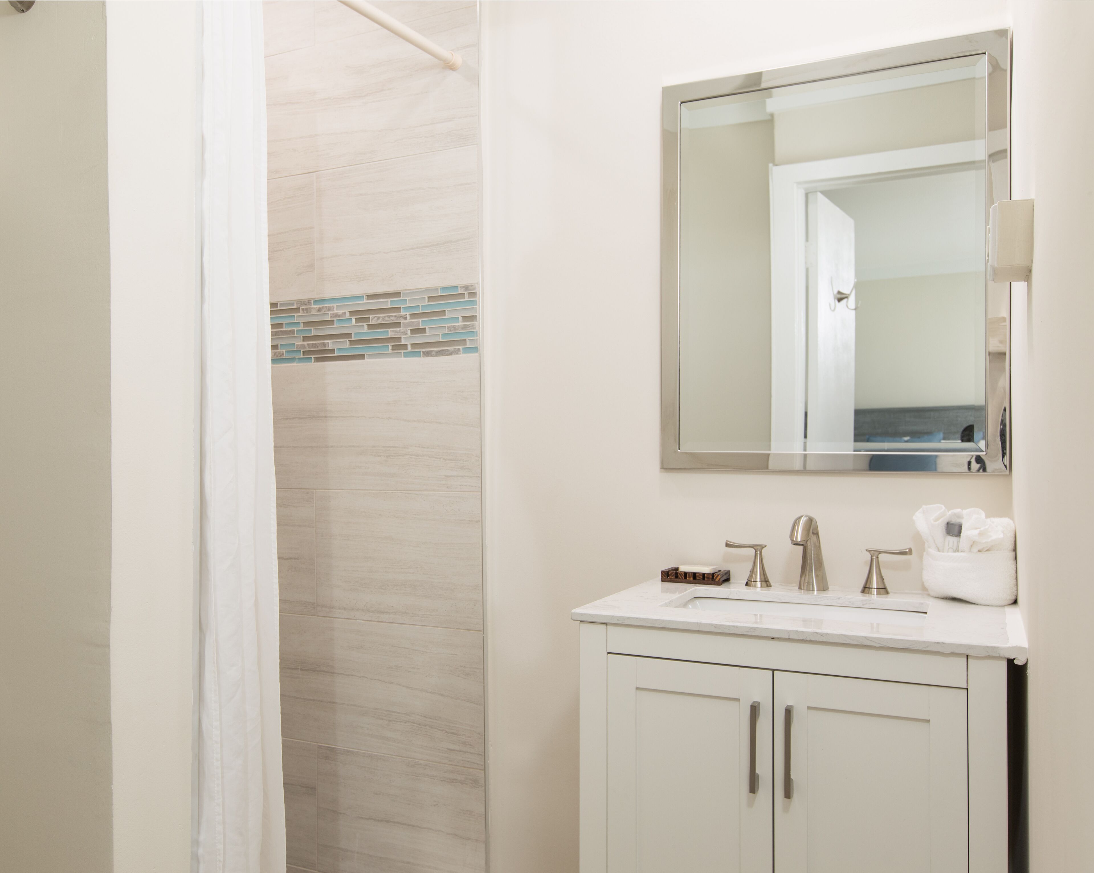 A bathroom with a shower, a sink with a mirror above it, and a towel rack.