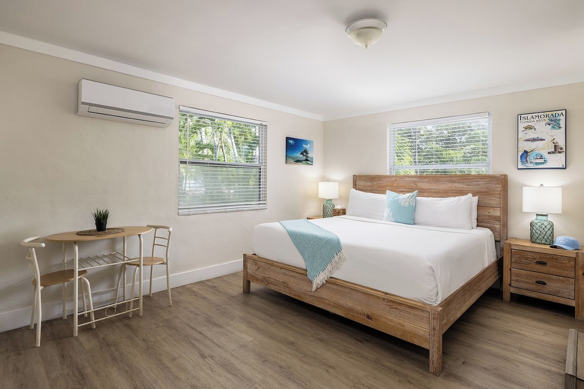A bedroom with a wooden bed, two bedside tables, a nightstand, a small desk with a chair, and a potted plant.