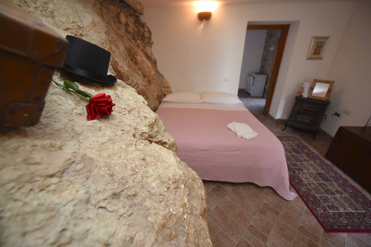 Een slaapkamer met een bed, een rode roos, een zwarte hoed en een wand met een structuur.