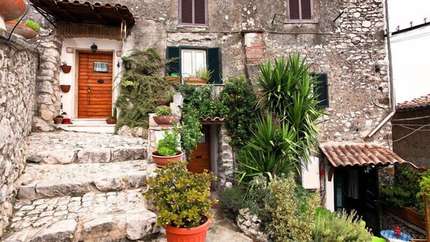 Un edificio de piedra con puerta de madera, plantas en macetas y un pequeño jardín.