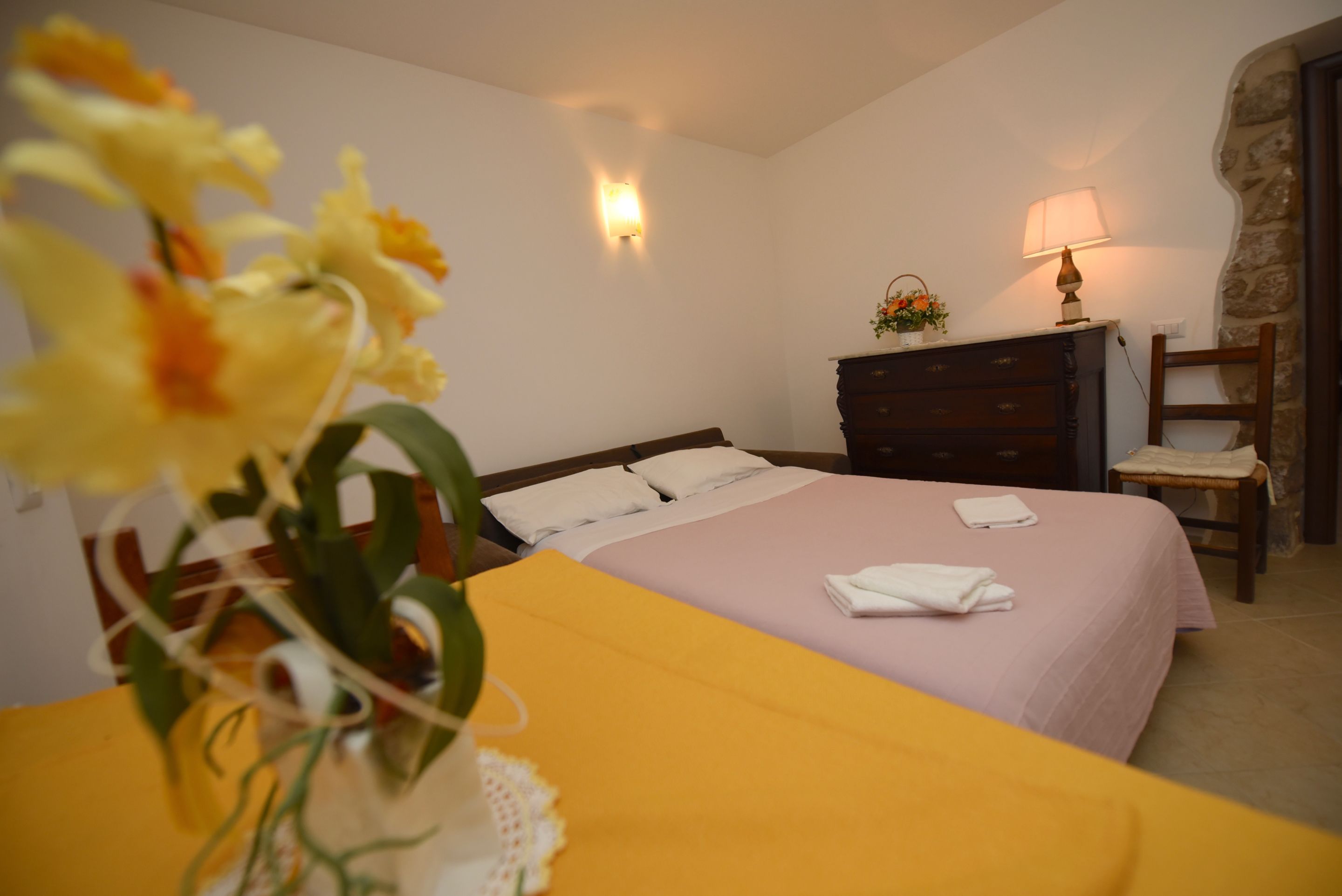 Ein Hotelzimmer mit Bett, einem hölzernen Schminktisch, einem Nachttisch, einer Lampe und einer Blumenvase.
