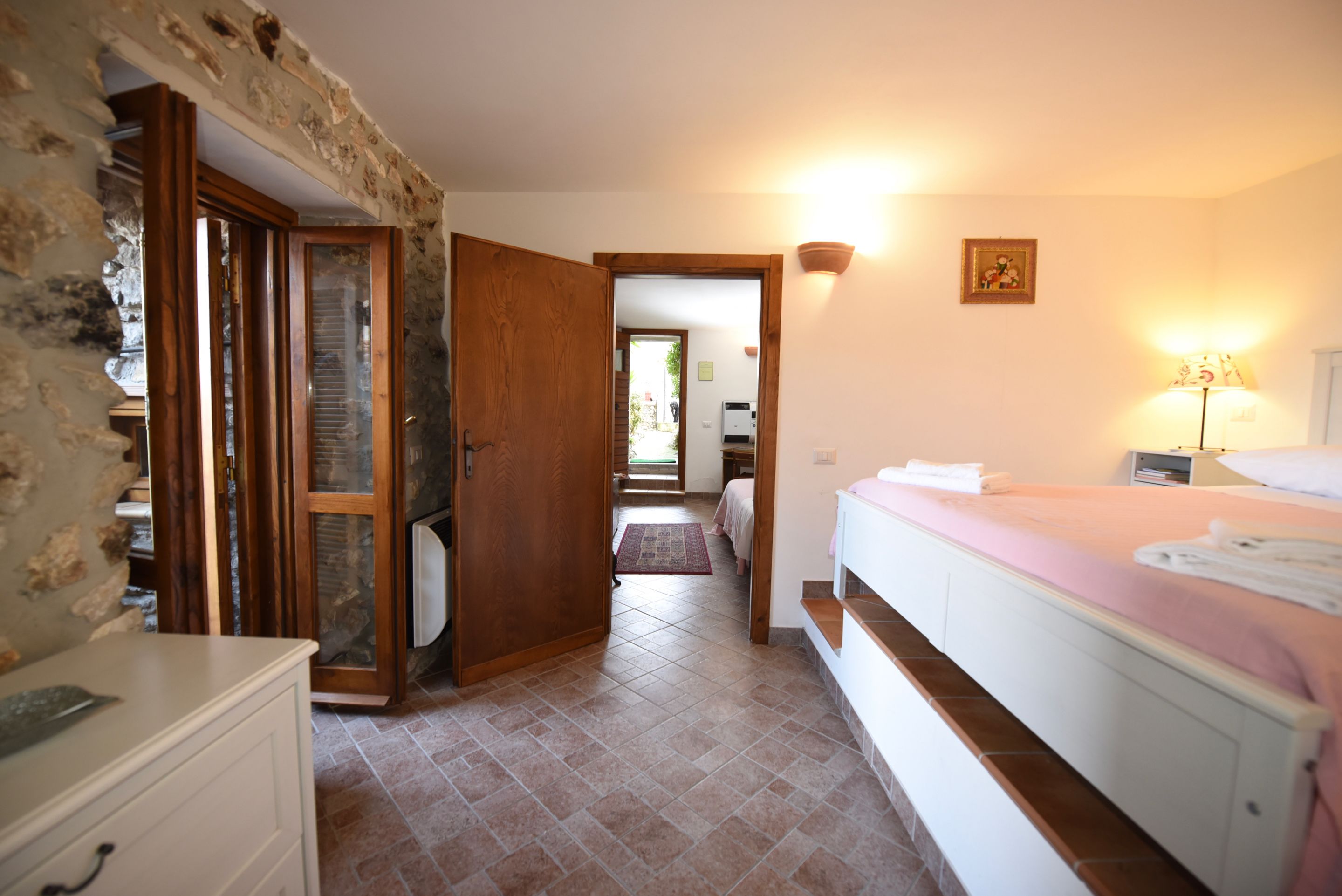 Une chambre à coucher avec un lit, une table de chevet, une lampe et une salle de bain visible à travers une porte ouverte.
