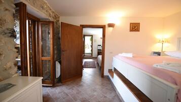 Une chambre à coucher avec un lit, une table de chevet, une lampe et une salle de bain visible à travers une porte ouverte.