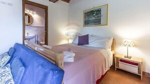 Un dormitorio con una cama, un banco de madera, una mesita de noche con una lámpara y un cuadro en la pared.