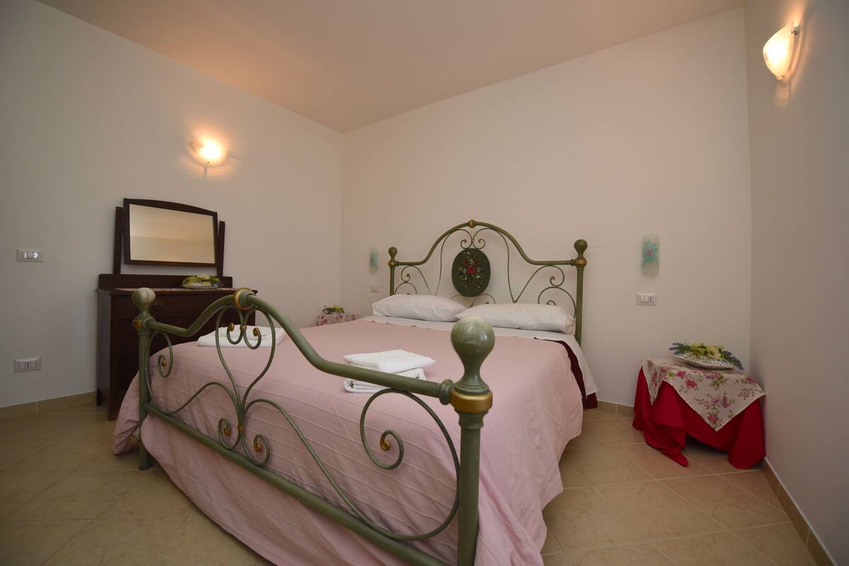Een slaapkamer met een bed, een dressoir, een nachtkastje en een tafel met een bloemenonderzetter.