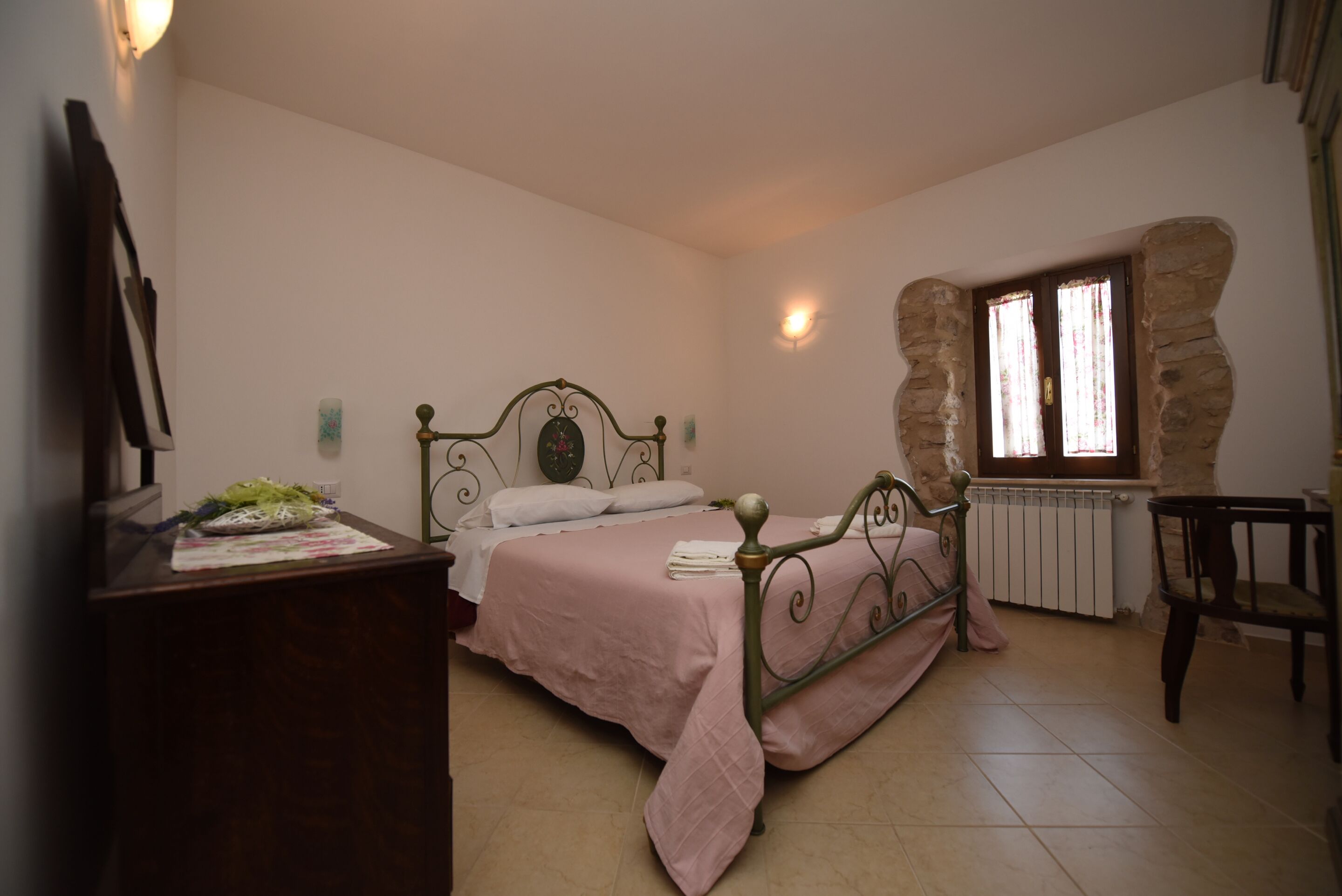 Een slaapkamer met een bed, een kaptafel, een stoel en een stenen muur.
