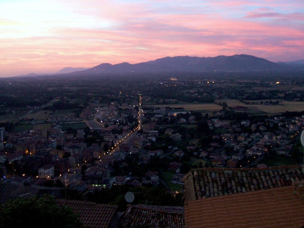 Une vue panoramique d’une ville au crépuscule, traversée par une rivière et entourée de montagnes.