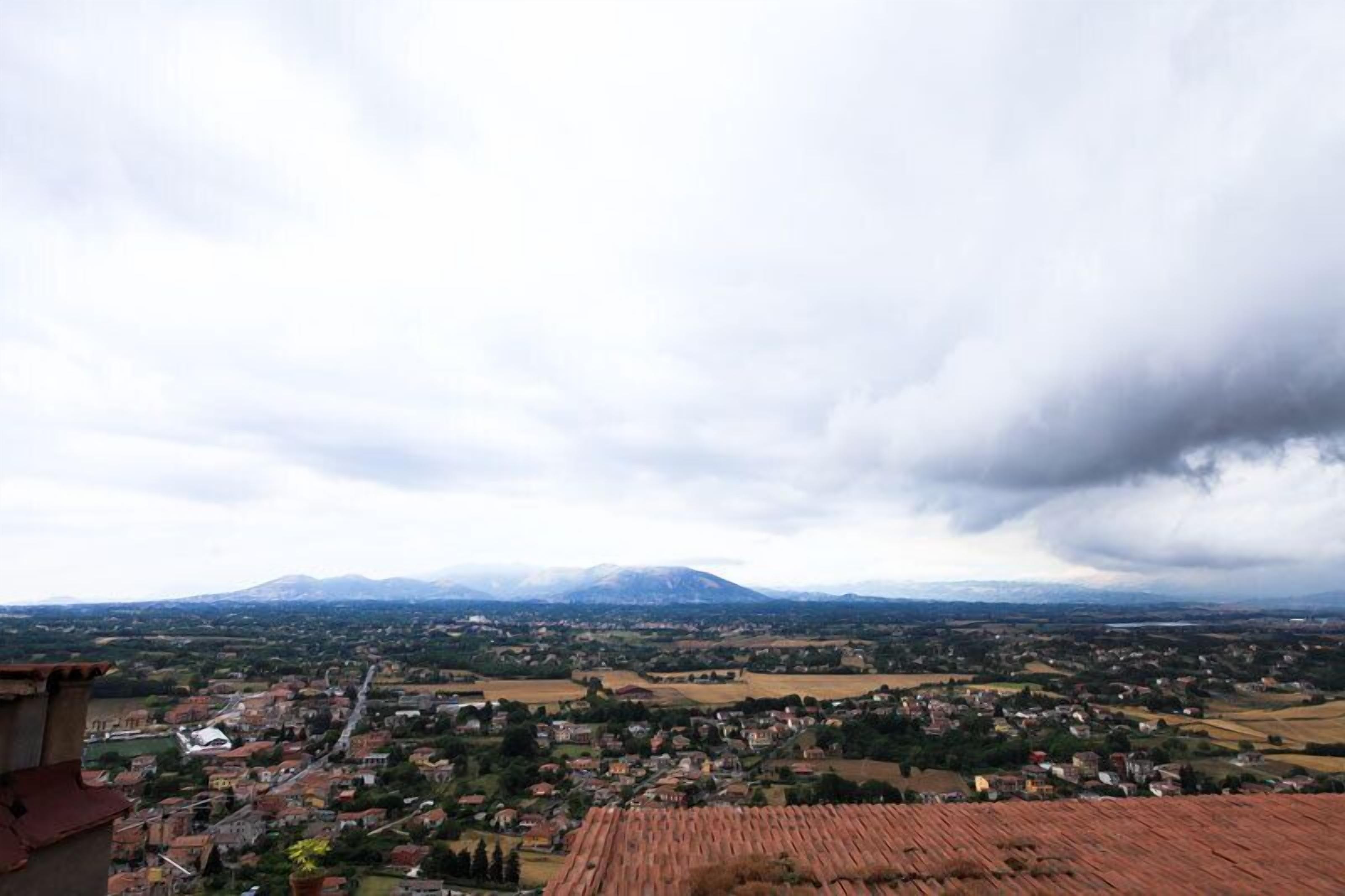 A panoramic view of a town with a mountain range in the background, featuring a mix of residential and agricultural areas.