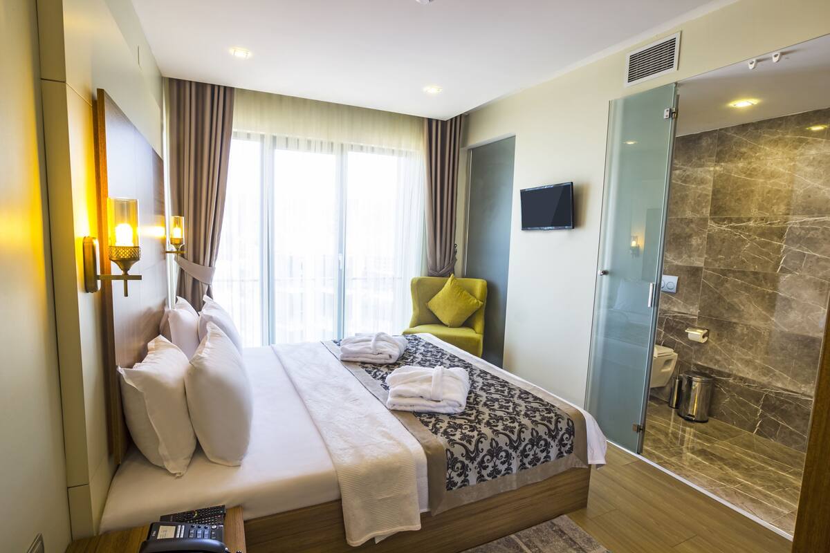 A hotel room with a bed, a green chair, a shower, and a television on the wall.