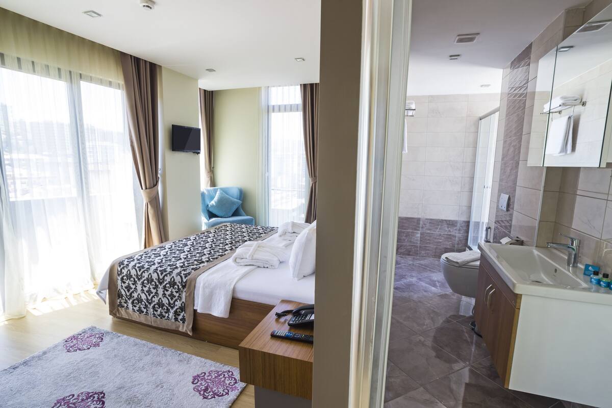 A hotel room with a bed, a TV, a bathroom with a sink and toilet, and a view of the city.