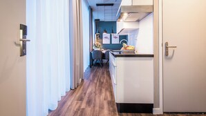 A modern kitchen with a wooden floor, white cabinets, and a dining area with chairs and a table. - YAYS Amsterdam North by Numa (Amsterdam)