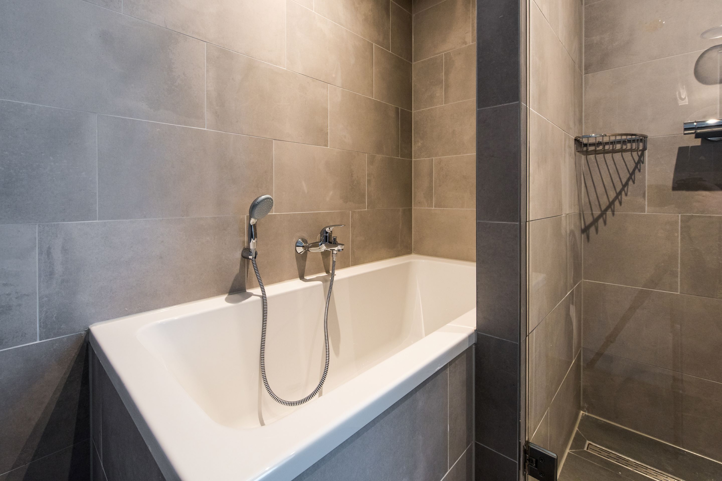 A modern bathroom with a white bathtub, a handheld showerhead, and a towel rack.