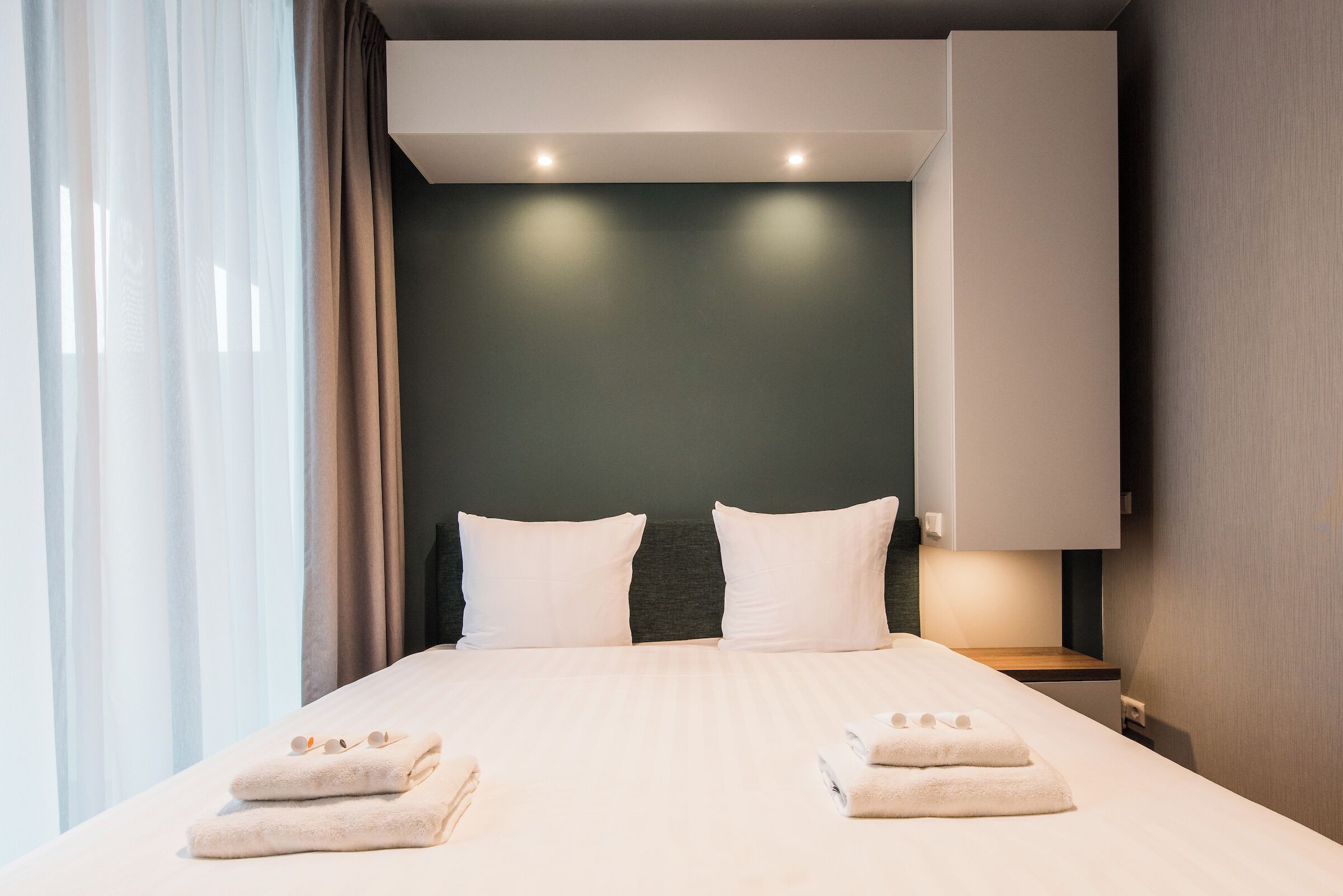 Ein modernes Hotelzimmer mit einem großen Bett, zwei Kissen, einem Nachttisch und einer Wandlampe.