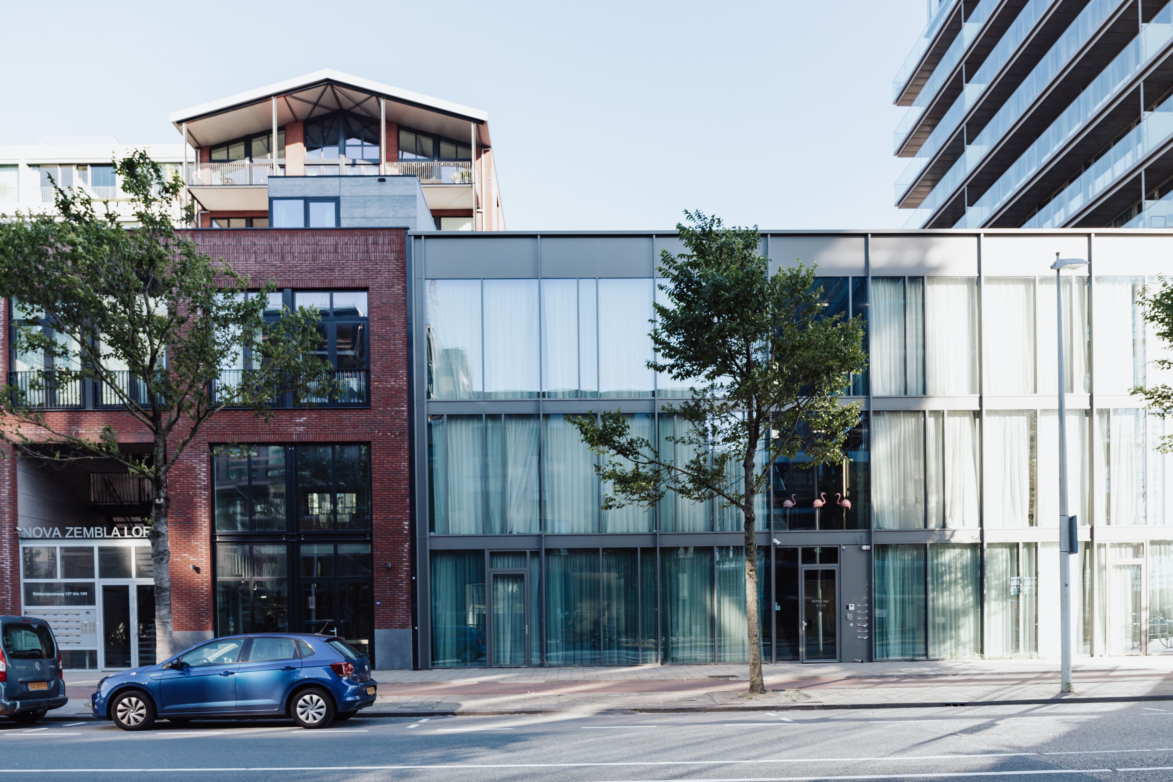 Un edificio moderno con facciata in vetro, ingresso ben visibile e un albero di fronte.