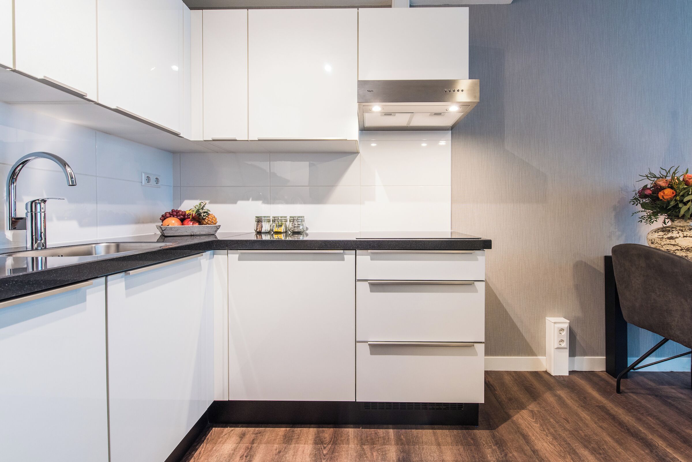 A modern kitchen with white cabinets, a stainless steel sink, and a black countertop.