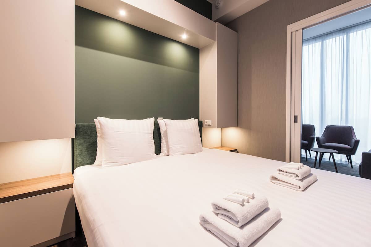 Een moderne hotelkamer met een opgemaakt bed, een nachtkastje, een stoel en uitzicht op de omgeving.