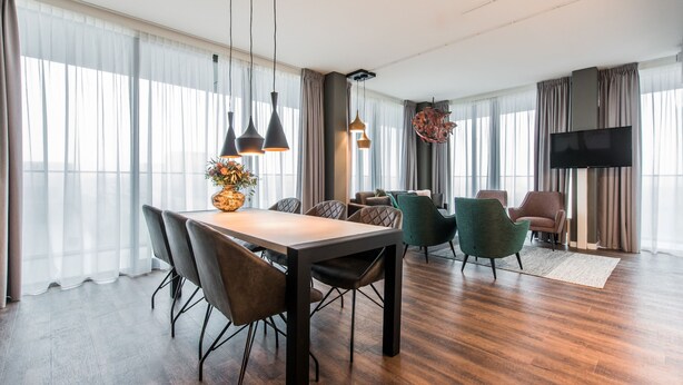 A modern hotel room with a dining area, a living area with a flat-screen TV, and large windows with sheer curtains. - YAYS Amsterdam North by Numa (Amsterdam)
