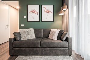 Un canapé gris agrémenté de coussins moelleux et à texture intéressante, une œuvre d’art représentant un flamant rose encadrée au mur et un luminaire suspendu moderne.