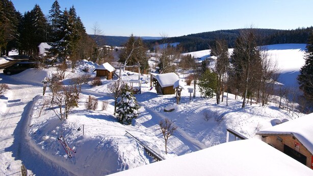 A snow-covered village with wooden houses, a clear sky, and a lake in the background. - Höhengasthaus Kolmenhof an der Donauquelle (Furtwangen)