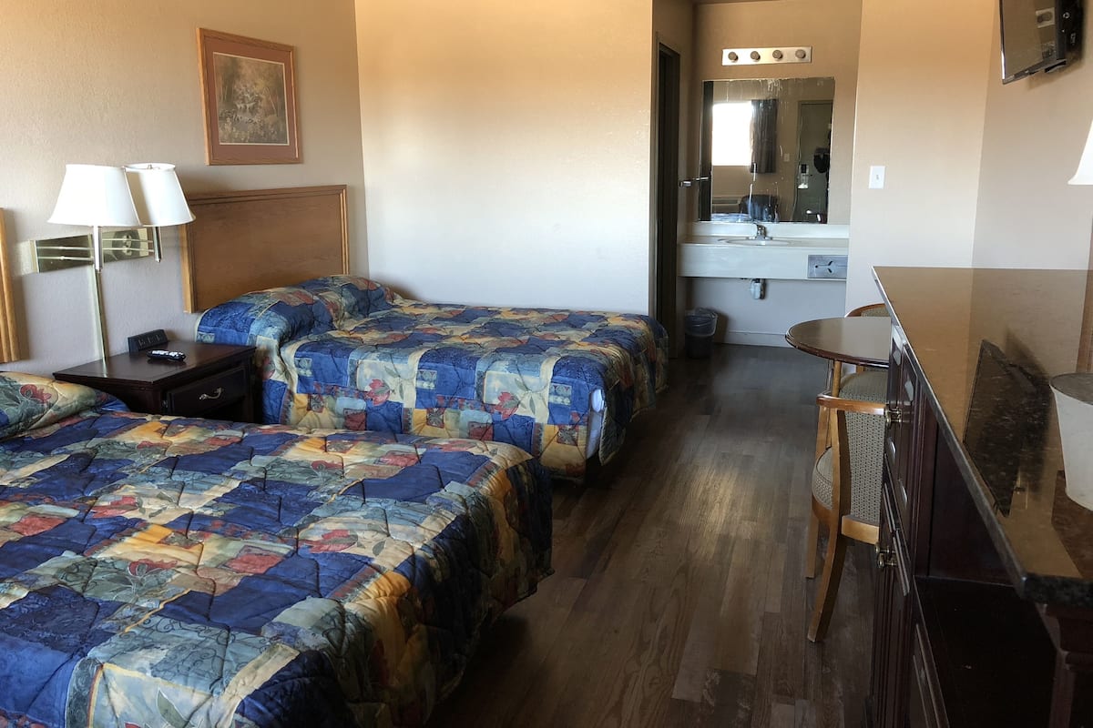 A hotel room with two beds, a desk, a chair, a mirror, and a small kitchenette.