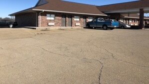 A motel with a brick facade, a covered parking area, and a blue pickup truck parked in front.