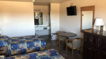 A hotel room with two beds, a small dining table, a TV, and a mirror.
