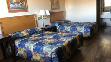 A hotel room with two beds, wooden headboards, a nightstand with a lamp, and framed artwork on the walls.