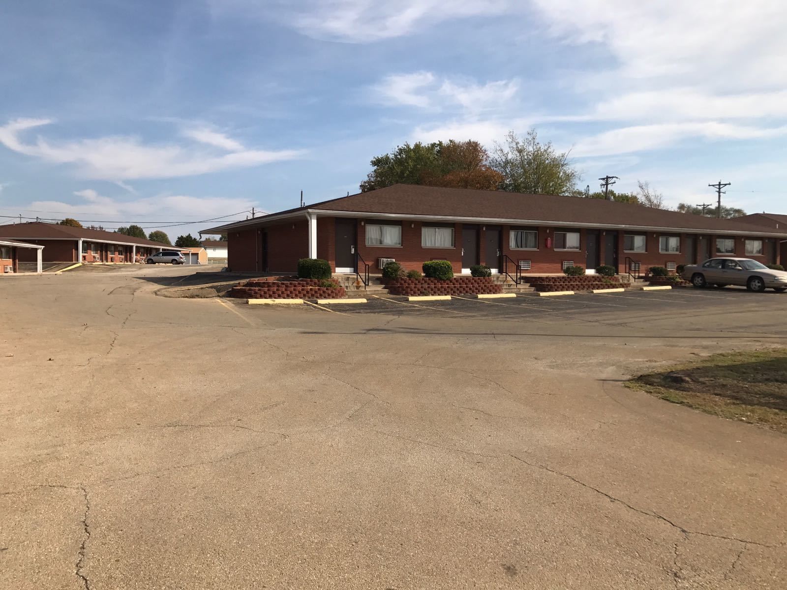 A motel with a parking lot, a brick building, and a few cars parked.