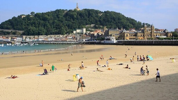A beach with people sunbathing and swimming, a hill with a statue, and buildings in the background. - Basic Confort 2 (San Sebastián)