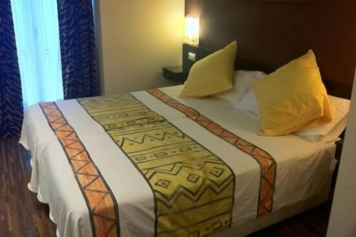 A hotel room with a bed, a nightstand, and a lamp.