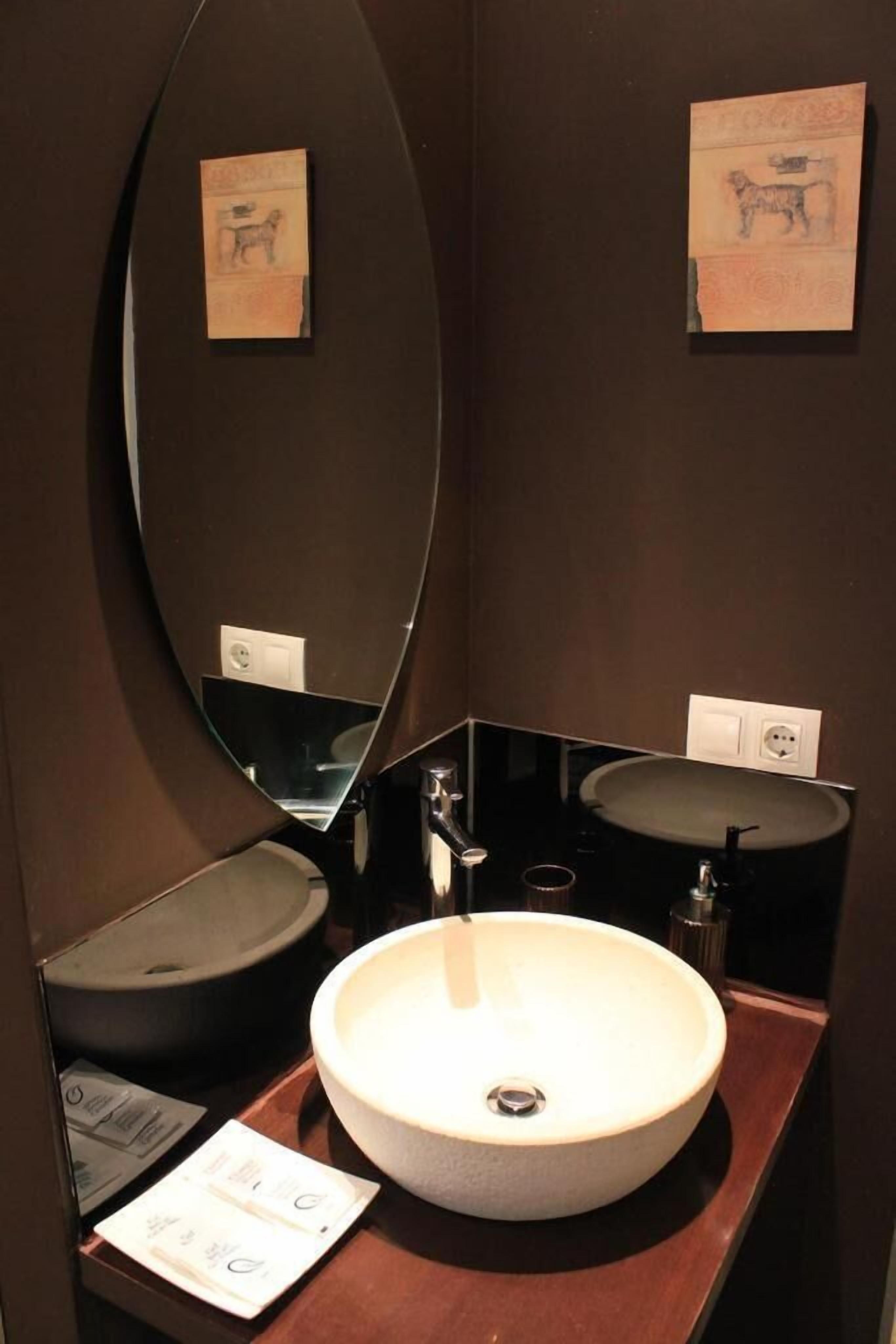 Un baño con un lavabo ovalado grande, dos lavabos más pequeños y un espejo.