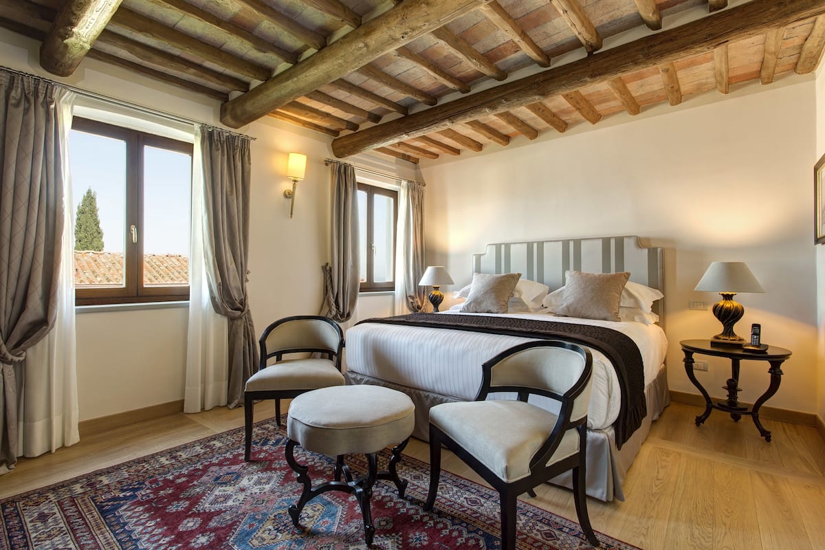 A bedroom with a large bed, two chairs, a nightstand, and a window with curtains.