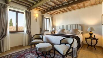 A bedroom with a large bed, two chairs, a nightstand, and a window with curtains.