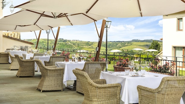 Un espace de restauration en plein air, avec des chaises et des tables en osier, des nappes blanches et des parasols, offrant une vue sur un paysage pittoresque.