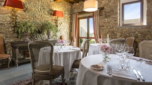 Un espace repas aux murs de pierre, avec des poutres en bois et des tables rondes dressées pour le repas.
