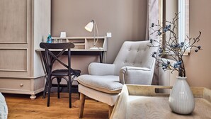 A room with a wooden floor, a desk with a lamp, a chair, a sofa, and a vase with branches. - Hotel Hollenstedter Hof (Hollenstedt)