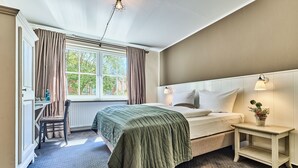 A bedroom with a bed, a bedside table with a lamp, a chair, and a window with curtains. - Hotel Hollenstedter Hof (Hollenstedt)