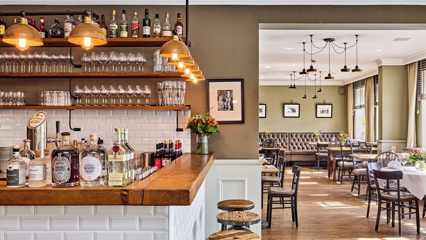 A bar area with shelves of liquor bottles and glasses, a wooden counter, and stools. - Hotel Hollenstedter Hof (Hollenstedt)